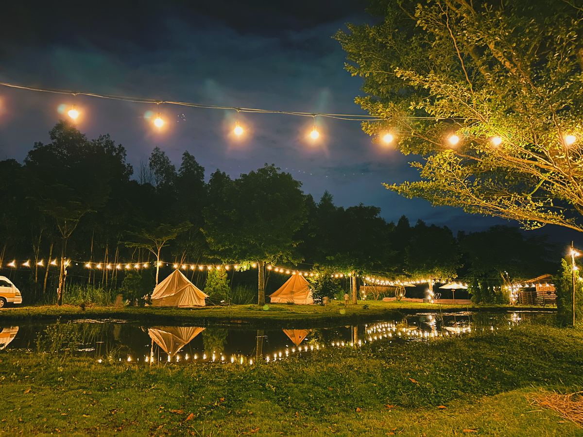 Khu cắm trại Sachi gần Sài Gòn về đêm — lều glamping, đèn dây và mặt hồ phản chiếu tại Nhơn Trạch